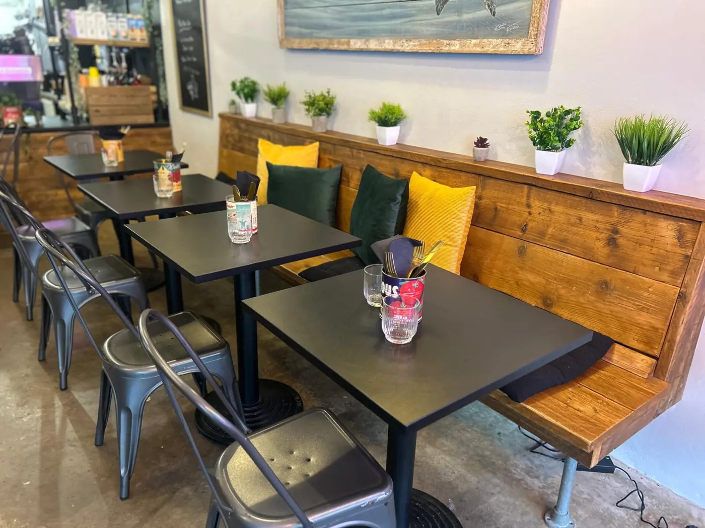 Inside Bru & Bear: a wooden bench with green and yellow cushions and small black tables