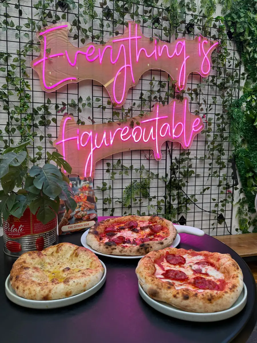 Three Neapolitan pizzas on a table under a pink neon sign